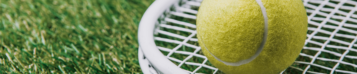 close up view of tennis ball on racket lying on green lawn